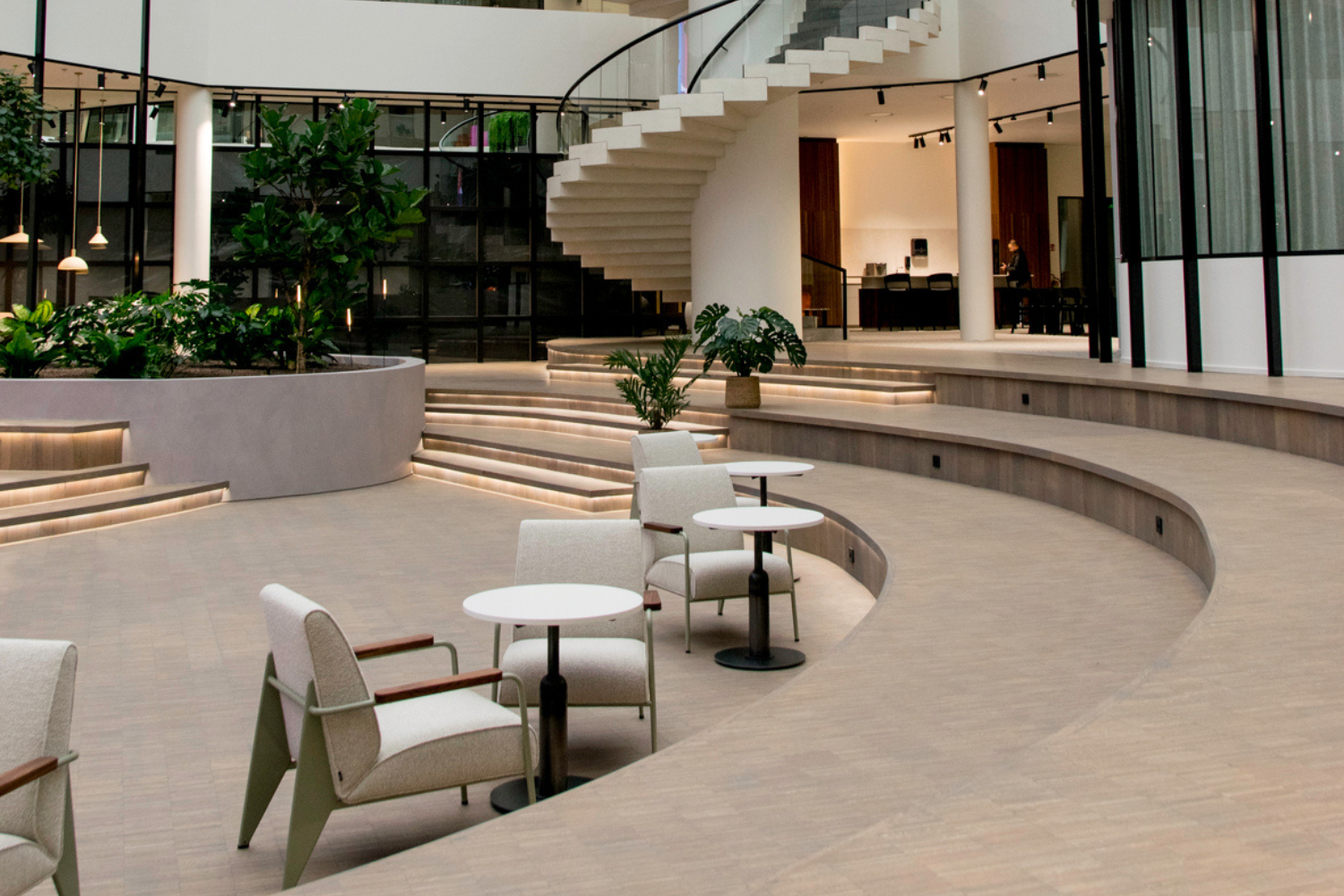 Moderne en stijlvolle kantooromgeving met een open indeling. Met een centrale trap, ronde zitbanken en tafeltjes met stoelen.