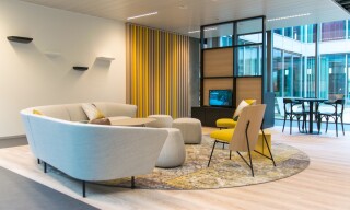Office design of lounge area with yellow colour accents and a grey sofa with matching poufs